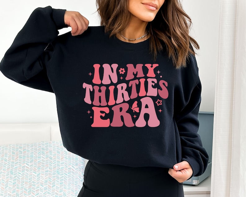 May include: Black sweatshirt with a pink and red graphic that says "In My Thirties Era" in a retro font.