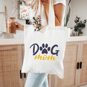 May include: White canvas tote bag with a blue paw print and the text "Dog Mom" in yellow letters.