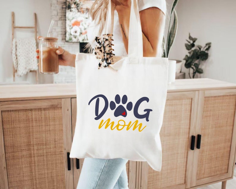 May include: White canvas tote bag with a blue paw print and the text "Dog Mom" in yellow letters.