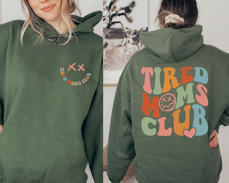 Puede incluir: Sudadera con capucha verde con un gr&aacute;fico colorido de "Tired Moms Club" en la espalda y una carita sonriente con el texto "Tired Moms Club" en la parte delantera.