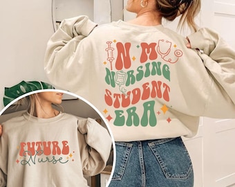 May include: Two beige sweatshirts with a retro-style graphic design. One sweatshirt says "Future Nurse" and the other says "In My Nursing Student Era".
