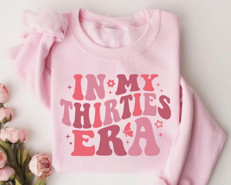 May include: Pink sweatshirt with the text "IN MY THIRTIES ERA" in a retro font with pink, red, and white colors.