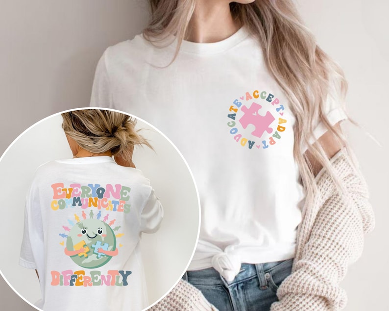 May include: White t-shirt with a colorful graphic on the back that says "Everyone Communicates Differently" and a colorful graphic on the front that says "Advocate Accept Adapt".