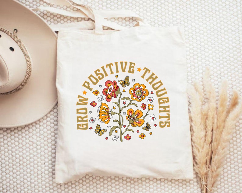 May include: A white canvas tote bag with a floral design and the text "Grow Positive Thoughts" in gold lettering.