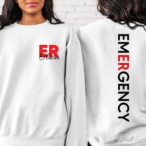 May include: White sweatshirt with the text "ER Olivia" in red and black on the front and "EMERGENCY" in black on the back.