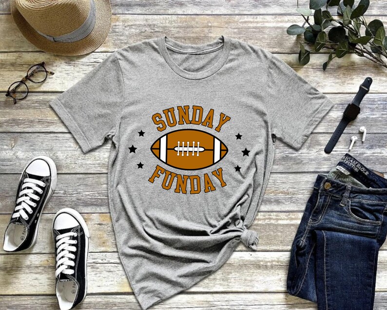 Pode incluir: Camiseta cinza com um gr&aacute;fico de futebol americano marrom e o texto "SUNDAY FUNDAY" em laranja.