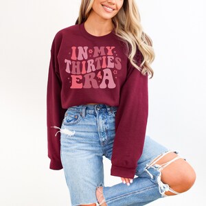 May include: A maroon sweatshirt with a pink and red graphic that says "In My Thirties Era" with stars and flowers around the text.