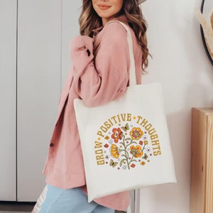 May include: A white tote bag with a floral design and the text "Grow Positive Thoughts" in yellow and orange lettering.