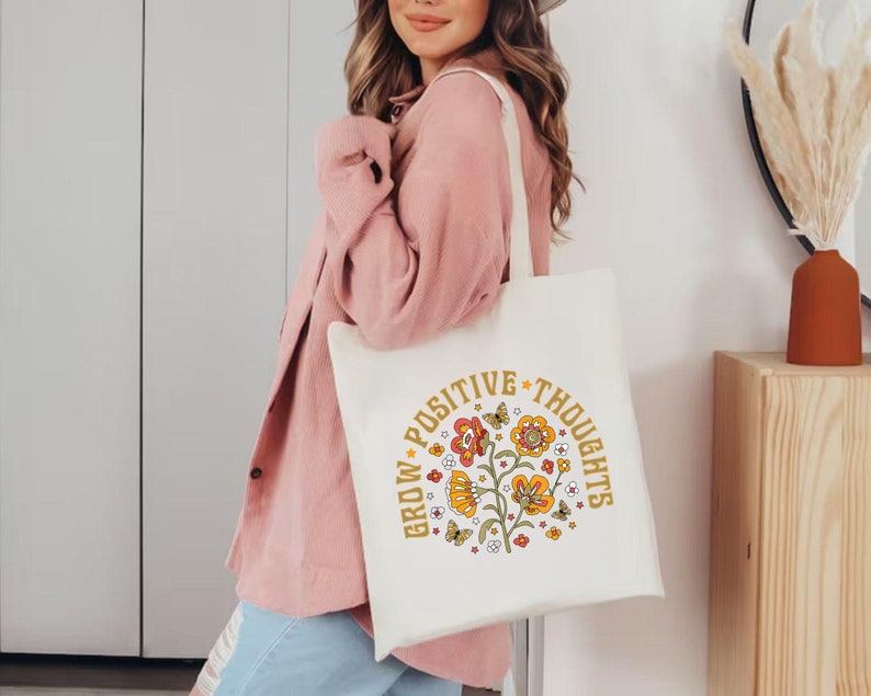 May include: A white tote bag with a floral design and the text "Grow Positive Thoughts" in yellow and orange lettering.