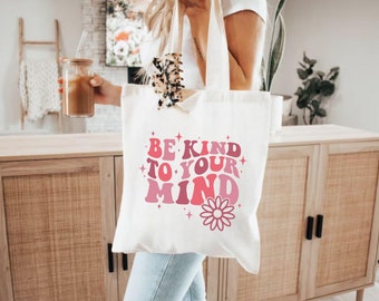 May include: White canvas tote bag with pink and red text that reads "Be Kind To Your Mind" with a pink flower graphic.