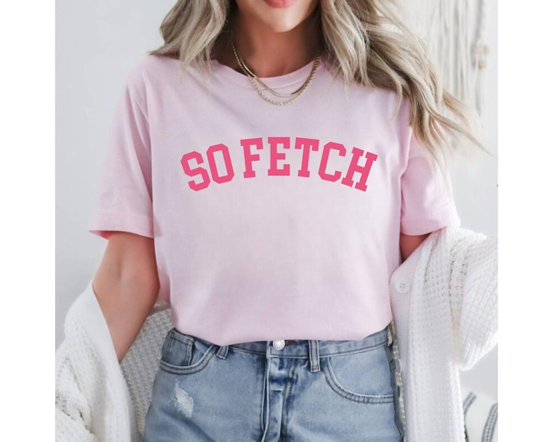 Op de afbeelding: Roze T-shirt met de tekst "SO FETCH" in een roze, universitaire stijl lettertype.