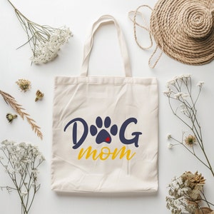 May include: A white canvas tote bag with a blue paw print and the text "Dog Mom" in yellow.