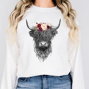 Puede incluir: Sudadera blanca con una ilustraci&oacute;n en blanco y negro de una vaca de las tierras altas con una corona floral de flores burdeos y rosas.