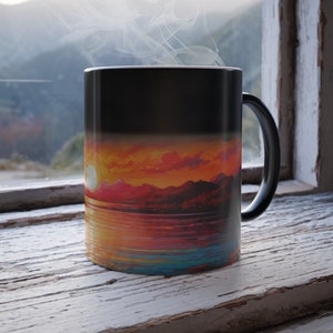 May include: A black ceramic mug with a heat-sensitive design. The mug is filled with a hot beverage, and steam is rising from the top. The design on the mug is a colorful sunset over a body of water with mountains in the background.