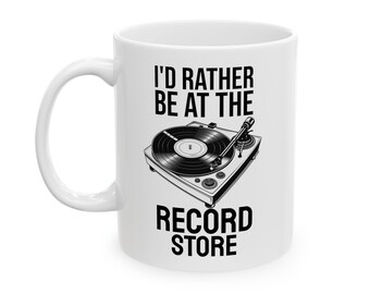 May include: White ceramic coffee mug with a black graphic of a record player and the text "I'd rather be at the record store".
