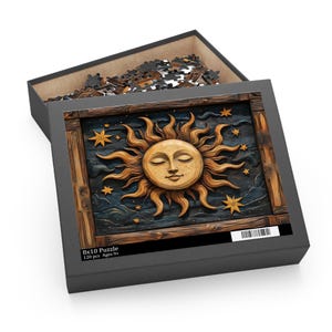May include: A puzzle box with a celestial design. The box is open, revealing puzzle pieces. The puzzle image features a sun with closed eyes, surrounded by star shapes, set against a dark blue background. The box reads "8x10 Puzzle 120 pcs Ages 9+".