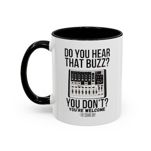 May include: White ceramic coffee mug with a black handle and black rim. The mug has a black and white image of a soundboard with the text "Do you hear that buzz? You don't? You're welcome - The Sound Guy".