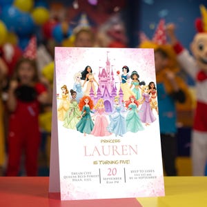 May include: A pink and white princess-themed birthday party invitation. The invitation features illustrations of various princesses in front of a castle. The text reads "Princess Lauren is turning five!" with event details.