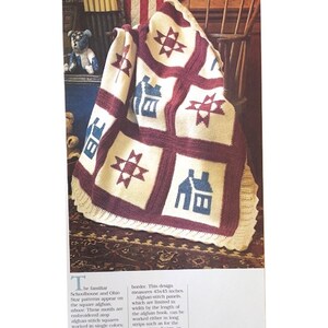Può includere: Una coperta all'uncinetto con uno schema di colori rosso, bianco e blu. La coperta presenta un motivo ripetitivo di stelle e case. La coperta misura 114,3 x 114,3 cm.