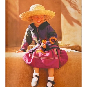 Op de afbeelding: Een jong meisje in een paarse, groene en gele trui, een roze rok en een strohoed zit op een stenen muur. Ze houdt een klein boeket bloemen vast.