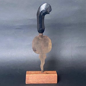 以下が含まれることがあります： 暗い曲線的なハンドルと、円形の古くなった木材要素を備えた手作りの木製彫刻。 長方形の木製ベースに取り付けられており、さまざまな質感と色合いを示しています。 高さ約20cm。