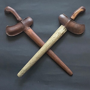 Peut inclure: Deux poignards en bois avec des poignées ornées et des lames croisées sur un fond gris foncé.