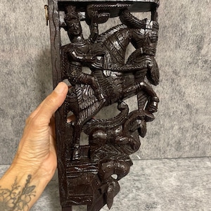 Peut inclure: Étagère murale en bois brun foncé, finement sculptée, représentant un relief détaillé d'une figure à cheval. La sculpture présente un design traditionnel avec des détails ornés, idéal pour ajouter une touche d'art culturel à tout espace.