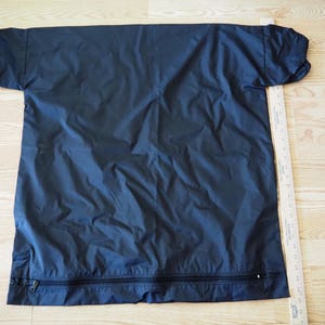 May include: A navy blue, short-sleeved garment with a full-length zipper at the bottom. The garment is laid flat on a wooden surface next to a ruler. The fabric appears to be lightweight and slightly wrinkled.