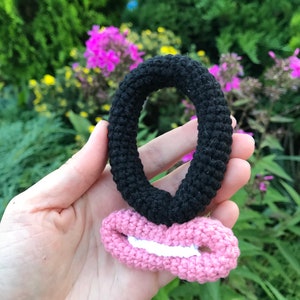 May include: A black crocheted hair scrunchie with a pink crocheted bow attached to it.