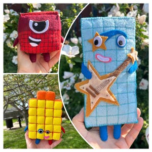 May include: Three plush toys inspired by Numberblocks characters. One is a red square with a single eye, one is a yellow rectangular block with multiple segments, and one is a light blue rectangular block holding a tan star-shaped guitar.