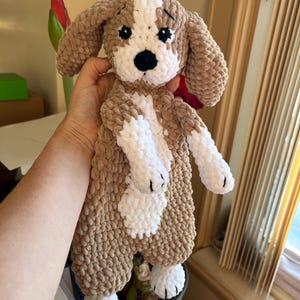 May include: A crocheted plush toy dog with brown and white fur. The dog has black eyes and a black nose. The dog is holding its paws up in the air.