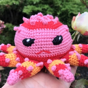 May include: A crocheted octopus plush toy with pink, red, and orange stripes. The octopus has black eyes and a small, stitched-on mouth.