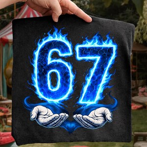 May include: Black square towel with the number 67 in bright blue flames. The number is outlined in blue with a lightning effect. Two hands are illustrated below the number, cupping the flames.