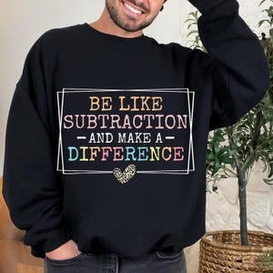 May include: Black sweatshirt featuring the text "BE LIKE SUBTRACTION - AND MAKE A - DIFFERENCE" in a rectangular frame. The text is multi-coloured, with a leopard print heart below.
