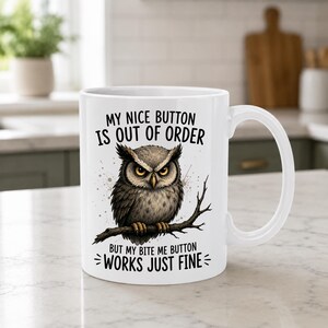 May include: A white ceramic mug featuring a graphic of a brown and grey owl perched on a branch. The text above the owl reads MY NICE BUTTON IS OUT OF ORDER and the text below reads BUT MY BITE ME BUTTON WORKS JUST FINE in black lettering.