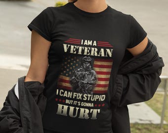 Puede incluir: Camiseta negra con el texto "I AM A VETERAN I CAN FIX STUPID BUT IT'S GONNA HURT" sobre una ilustración de un soldado y la bandera estadounidense. La camiseta la lleva una persona con gafas de sol.