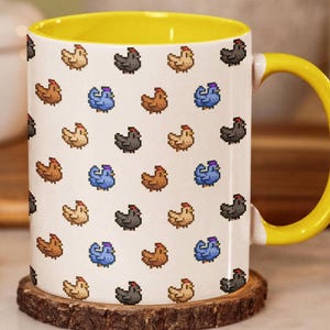 May include: A white ceramic mug featuring a repeating pixel art pattern of small chickens in shades of brown, blue, and black. The mug has a bright yellow interior and a matching yellow handle, providing a vibrant contrast to the white exterior.