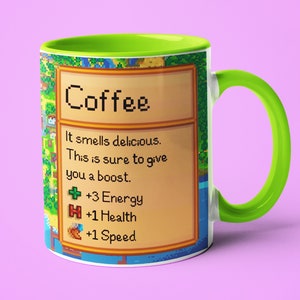 May include: A white coffee mug with a green rim and handle. The mug features a pixelated design inspired by the video game Stardew Valley. The design includes the text "Coffee" and a description of the coffee's effects: "It smells delicious. This is sure to give you a boost. +3 Energy, +1 Health, +1 Speed."