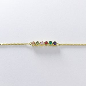 Puede incluir: Un brazalete de cadena dorada con siete piedras preciosas de colores. Las piedras preciosas est&aacute;n dispuestas en l&iacute;nea y son de los colores del arco&iacute;ris.