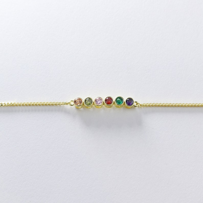 Puede incluir: Un brazalete de cadena dorada con siete piedras preciosas de colores. Las piedras preciosas est&aacute;n dispuestas en l&iacute;nea y son de los colores del arco&iacute;ris.