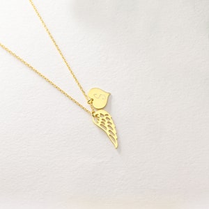 Pu&ograve; includere: Una collana color oro con una catena sottile. Il ciondolo presenta un cuore con la lettera "S" incisa e un ciondolo a forma di ala stilizzata. La collana &egrave; esposta su uno sfondo bianco.