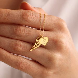 Pu&ograve; includere: Una collana dorata con un ciondolo a forma di ala e un ciondolo a forma di cuore con la lettera "S". La catena &egrave; sottile e la collana &egrave; mostrata su uno sfondo neutro.