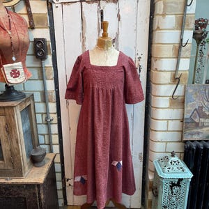 May include: A long, burgundy dress with a square neckline and short sleeves. The dress has a gathered skirt and is decorated with patchwork fabric on the bottom.