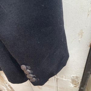 May include: A black blazer with a single button cuff. The blazer has a smooth, textured fabric.