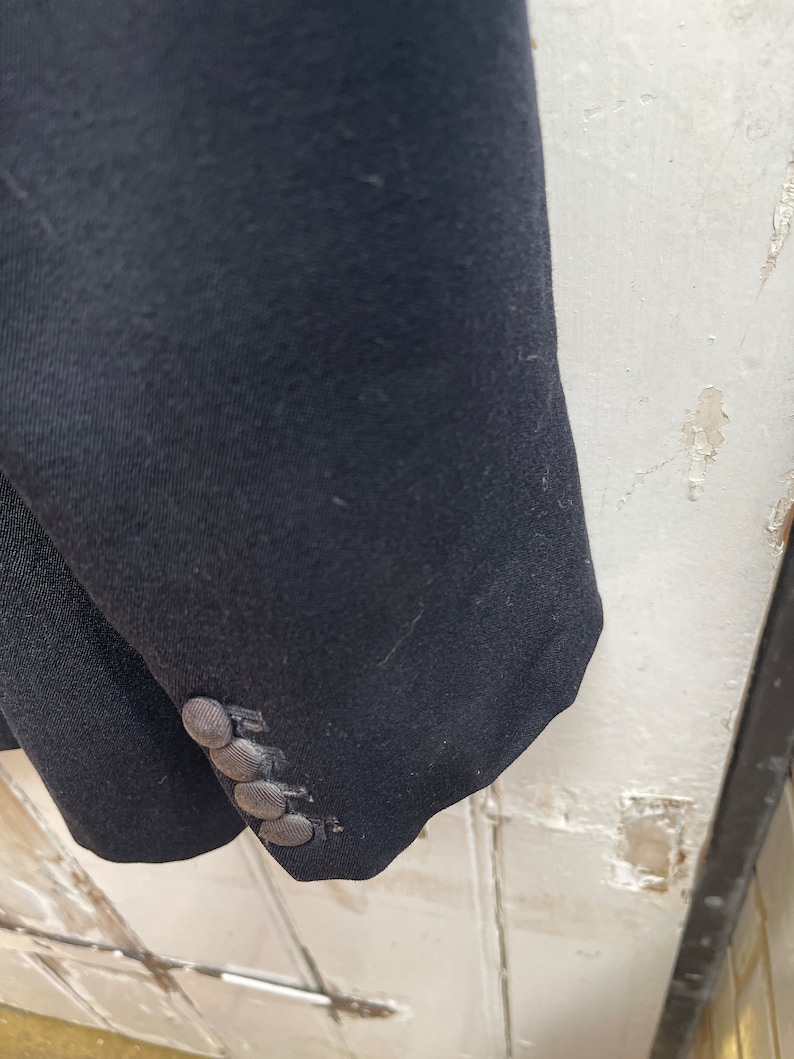 May include: A black blazer with a single button cuff. The blazer has a smooth, textured fabric.