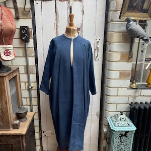 Peut inclure: Une robe tunique en lin bleu foncé avec un décolleté en forme de trou de serrure et des manches longues. La robe est exposée sur un mannequin dans un magasin.
