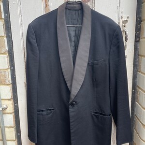May include: A black tuxedo jacket with a satin shawl collar. The jacket has a single button closure and two flap pockets.