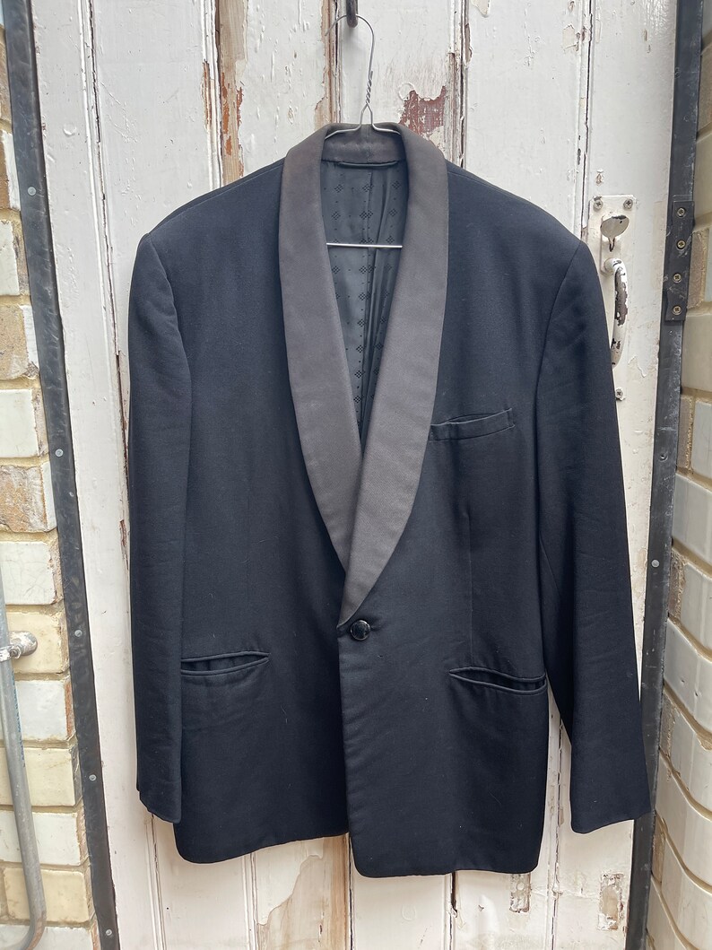 May include: A black tuxedo jacket with a satin shawl collar. The jacket has a single button closure and two flap pockets.