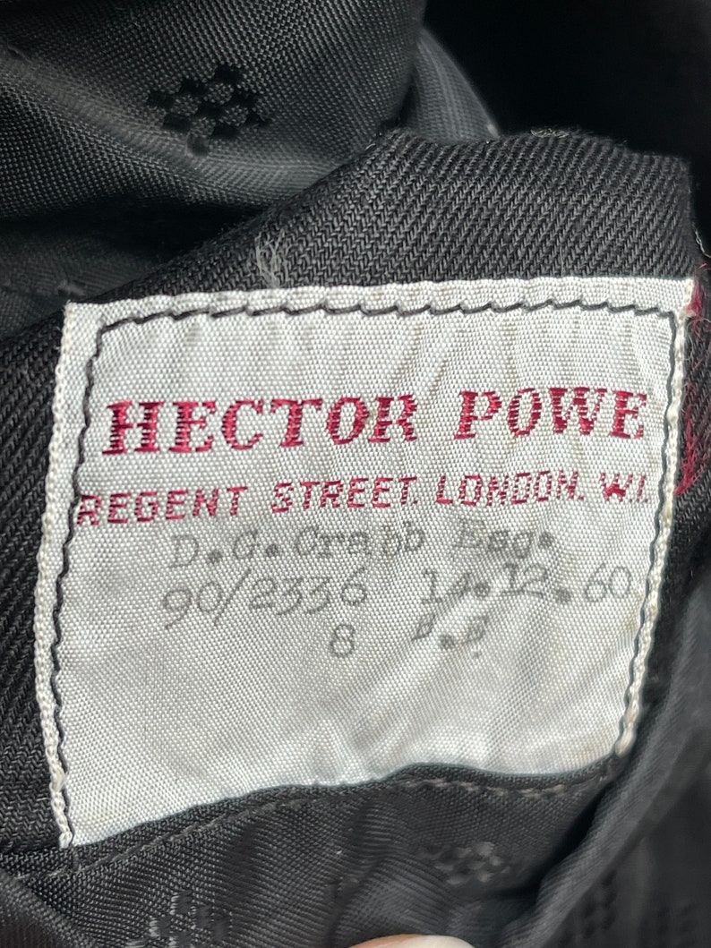 May include: A white label with black stitching and red text that reads "HECTOR POWE REGENT STREET LONDON W.1.  D.G.C. 90/2336 12.60"