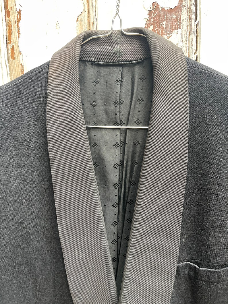 May include: A black tuxedo jacket with a satin lapel. The jacket is hanging on a hanger.